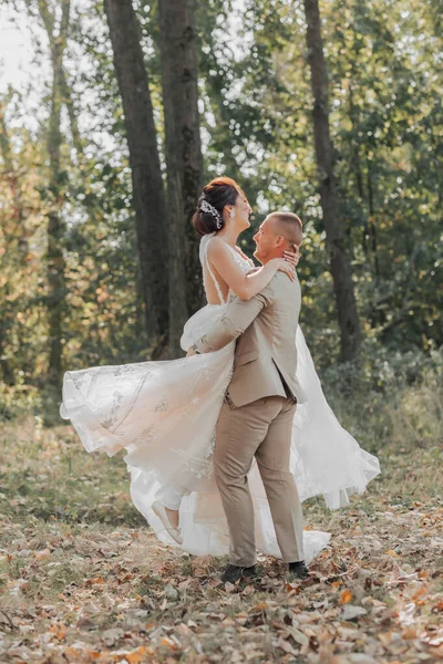 森林里幸福的新娘和新郎的画像 新郎把新娘抱在怀里 和她跳舞 连衣裙在运动的照片 婚纱照会 — 图库照片
