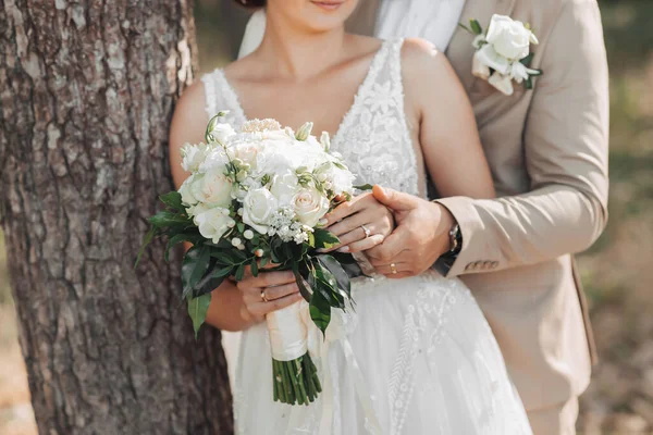 新娘和新郎手中拿着一束白花和绿叶的婚礼花的照片 新郎握住新娘的手 漂亮的手法国修指甲 结婚戒指 — 图库照片