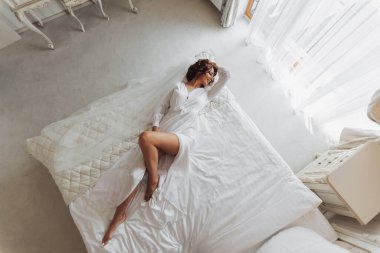 Beyaz peignoir giymiş güzel bir gelin otel odasında yatakta yatıyor. Düğün için son hazırlıklar. Gelin, damadı bekliyor. Günaydın, gelin. Yukarıdan Fotoğraf