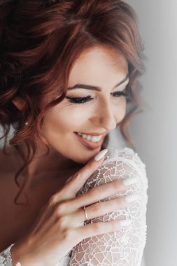 Güzel elbiseli gelin pencerenin yanında durup fotoğrafçıya poz veriyor. Düğün için. Düğün buketi Gelinin Sabahı. Mutlu bir gelin damadı bekliyor..