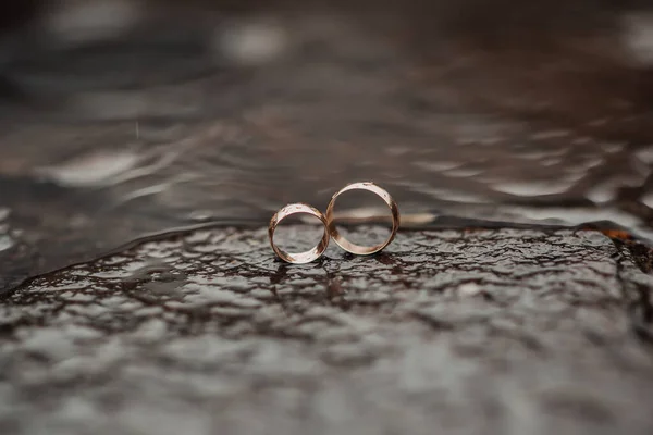 結婚式の写真 結婚指輪は水の中の石の上に立つ 背景がぼやけている 結婚式の詳細 茶色の背景 — ストック写真
