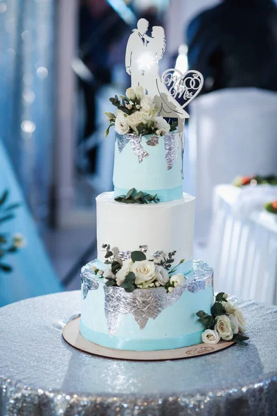 stock image A blue and white wedding cake, decorated with flowers and silver, stands on a silver stand. Decoration in the form of brides. flowers Wedding. Sweets