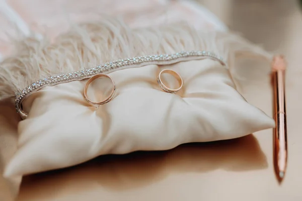 结婚戒指矗立在饰有羽毛的米黄色枕头上 结婚配件 婚礼的准备工作 — 图库照片