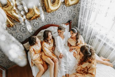 Bir otel odasında ipek bornozlu genç nedimeler. Bekarlığa veda partisini kutlayan güzel kadınlar temalı pijamalarıyla yatakta oturuyorlar..