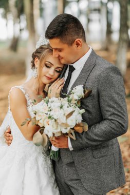 Gelin ve damat bir peri masalı ormanının arka planında. Kraliyet düğünü konsepti. Damat gelini kucaklıyor. Şefkat ve sakinlik