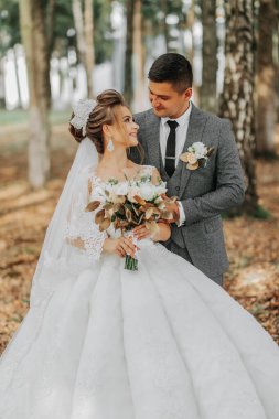 Gelin ve damat bir peri masalı ormanının arka planında. Kraliyet düğünü konsepti. Damat gelini kucaklıyor. Şefkat ve sakinlik. Portre fotoğrafı