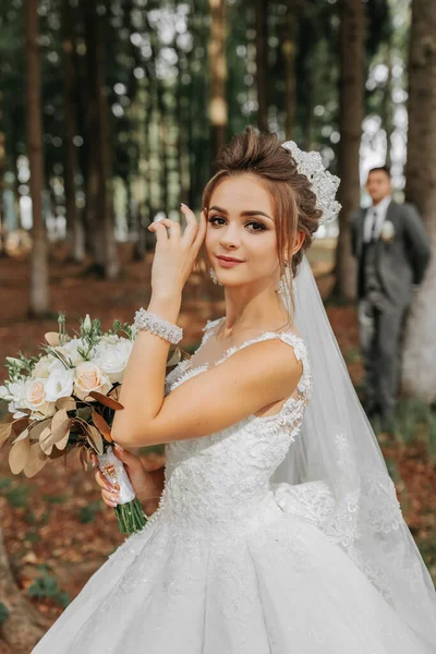 아름다운 드레스를 스타일의 나무들 사이에 아름다운 꽃다발을 티아라 황금빛 결혼식 — 스톡 사진