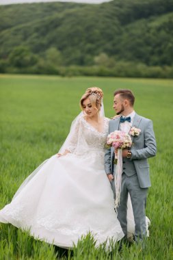 Yeni evliler sahada durup birbirlerine bakıyorlar. Gelin bir buket tutuyor. Doğada düğün. Gelin ve damadın portresi. Şık damat