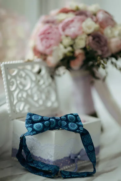 新郎的蓝色蝴蝶站在一个木制的盒子上 盒子上有结婚戒指 背景是一束婚纱 结婚细节 — 图库照片