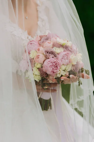 照片上是一束粉红色的牡丹 新娘站在那里 手里拿着一束鲜花 穿着白色的连衣裙 头戴面纱 一件漂亮的衣服漂亮的女人婚纱照 — 图库照片