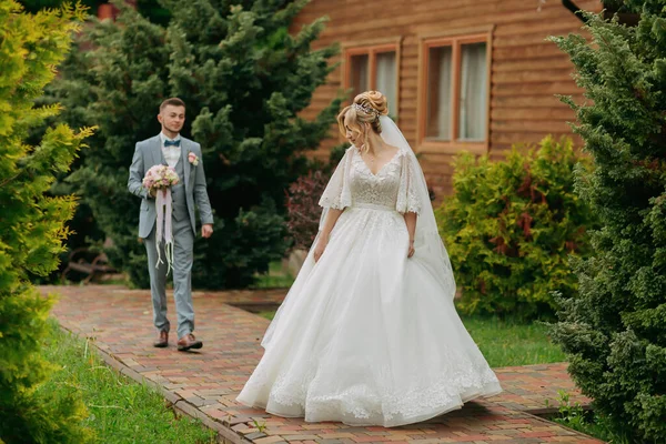 在大自然中举行婚礼新娘站在新郎的前面 从他的肩上望望树后和一个木棚屋 时髦的新郎 漂亮的新娘 — 图库照片