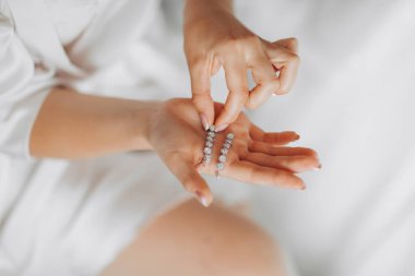 Düğün detaylarının fotoğrafı. Gelin gümüş elmas küpelerini tutuyor. Yukarıdan bak. Fransız manikürü. Güzel eller.