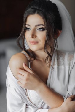 Cüppeli esmer gelin, kameraya poz veriyor, yana bakıyor. Omuzlarını aç. Şık saç stili. Güzel makyaj. Gönüllü duvak. Gelinin sabahı. Gelinin güzel elleri