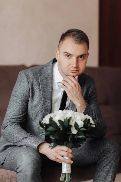 肖像画 白いシャツ 黒いネクタイ 灰色のスーツの男がソファに座って 白いバラの花束を持っています スタイリッシュな時計です 男性のスタイル ファッションだ — ストック写真