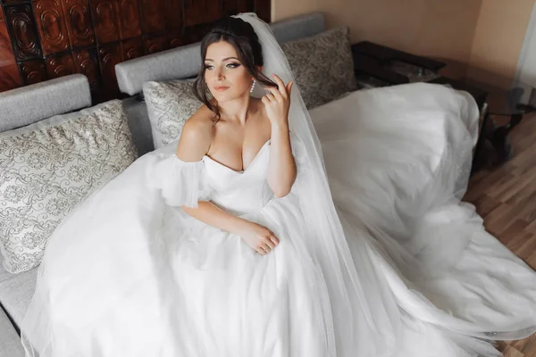Egy Barna Menyasszony Fehér Ruhában Pózol Miközben Egy Szürke Kanapén — Stock Fotó