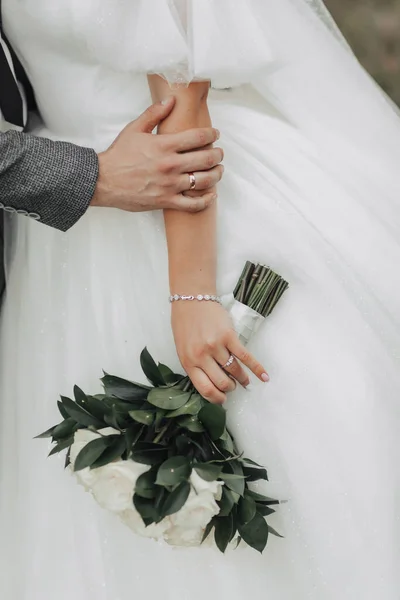 婚纱照的细节一束玫瑰和绿叶的照片 被新娘美丽的握住 新郎的手放在新娘的手上 手上的银质珠宝 — 图库照片