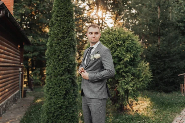 A man in a gray suit poses in nature, adjusts his tie. Side view. A stylish watch. Men's style. Fashion. Business.