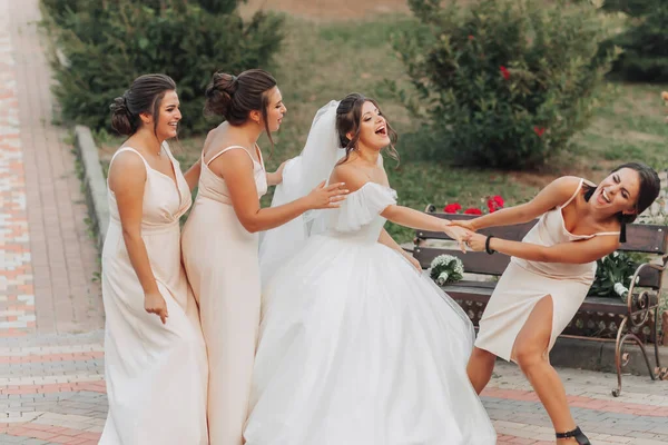 自然の中で結婚式の写真 白い長いドレスを着たブルネットの花嫁とヌードドレスの彼女の友人は一緒に周りをばかにし 誠実に笑っています 若い女性だ — ストック写真
