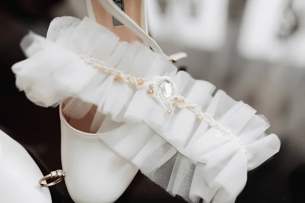 白色优雅的鞋子 新娘的结婚戒指夹在一双白色经典鞋子之间 新娘腿上的绷带系在鞋子上 集中在焦点上 婚纱照 — 图库照片