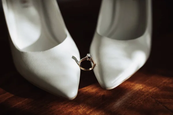 結婚式での詳細の写真 花嫁の結婚指輪は木製の背景にある白い古典的な靴の上に立つ 輪郭線だ 影と光 — ストック写真