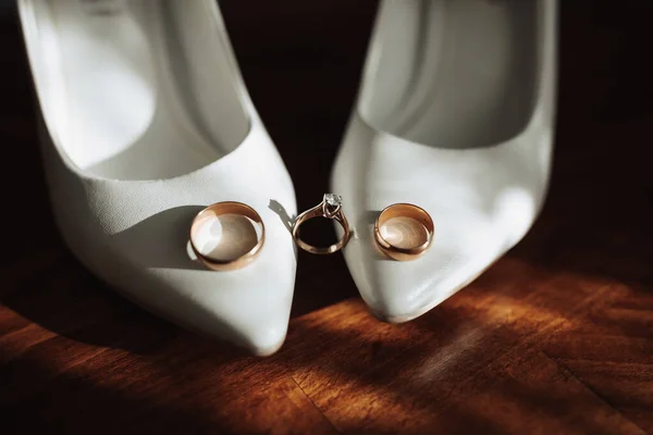 結婚式での詳細の写真 花嫁と新郎の結婚指輪は 木製の背景に位置して白い古典的な靴 上に立つ 輪郭線だ 影と光 — ストック写真