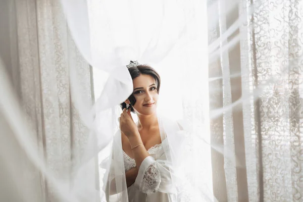一个黑发新娘裹着面纱站在窗边朝下看 漂亮的妆容和头发厚的面纱 婚纱照漂亮的新娘 — 图库照片