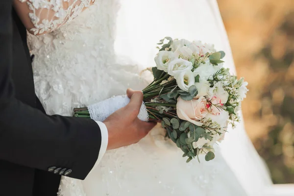 切り取られた結婚式の写真の詳細 黒のスーツの新郎とシックな白いドレスの花嫁は結婚式の花束を持っています 美しい手だ 肖像画 明るい夏の結婚式 — ストック写真