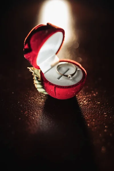 赤い箱の中に宝石を持つ花嫁の銀の婚約指輪は輪郭線の光でテーブルの上に立っています 結婚式の詳細の写真 — ストック写真