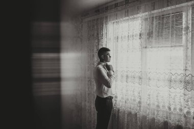 siyah beyaz fotoğraf. Yakışıklı adam beyaz bir gömleğin kolunu ilikler ve kameraya poz verir. Ön manzara. Gün ışığı. Moda ve tarz. İş için. Erkek tarzı. Güzel eller.