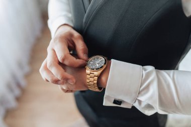 Erkek aksesuarları. Bir adam altın saatini ayarlar, yakın plan fotoğrafını. Erkek modası ve tarzı. İş için. Pahalı bir saat.