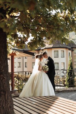 Düğün portresi. Doğada düğün töreni resmi. Damat bir buket tutuyor ve geline bakıyor, gelin damadın alyansını takıyor. Güzel altın kemer ve taze çiçekler