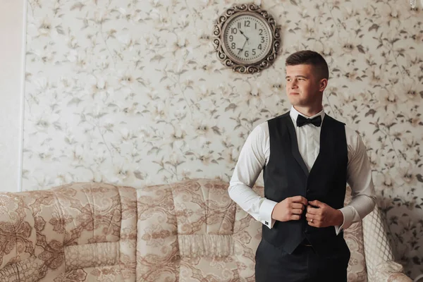 一个穿着白衬衫 黑色领结 黑色裤子和背心的男人在房间里摆姿势 一个时髦的手表 男人的风格 — 图库照片