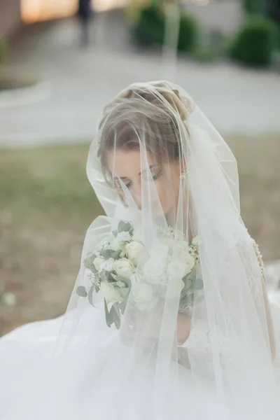 身穿白裙 头戴面纱的金发卷曲新娘 拿着一束玫瑰向镜头摆姿势 新娘的画像 漂亮的妆容和头发1 自然结婚 — 图库照片