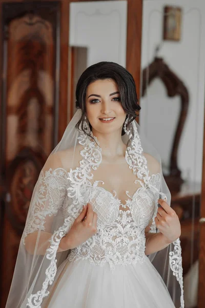 白いドレスを着たブルネットの花嫁と長いベールが窓のそばに立ってポーズをとっています 美しい手だ フランスのマニキュア 美しい髪とメイク — ストック写真
