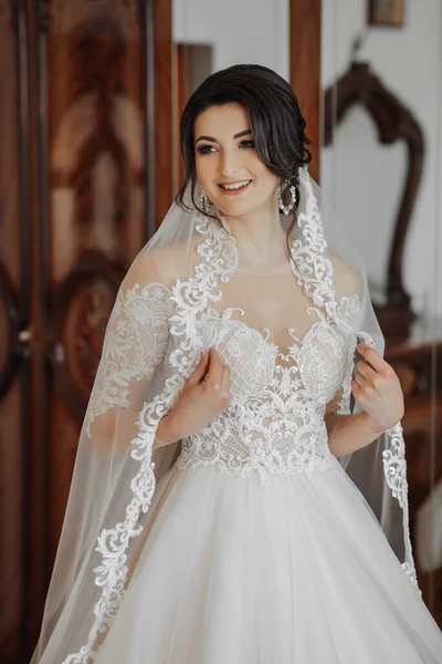 白いドレスを着たブルネットの花嫁と長いベールが窓のそばに立ってポーズをとっています 美しい手だ フランスのマニキュア 美しい髪とメイク — ストック写真