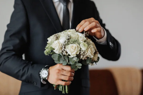 Portrait. A man in a white shirt, black bow tie and black tie poses in a room with a wedding bouquet. A stylish watch. Men\'s style. Fashion. Business