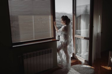 Güzel bir gelin nazikçe gülümser. Beyaz bir arka planda düğün saç stili. Genç ve güzel bir gelinin yakın plan portresi. Düğün için. İlginç bir ışık altında güzel bir gelin portresi