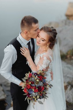 Nehrin kıyısındaki gelinler, çıplak bacaklarıyla bir kayanın üzerinde sarılırken ve öpüşürken ellerinde bir buket çiçek, kırmızı güller ve mavi çiçekler ve uzun beyaz bir elbise vardı.