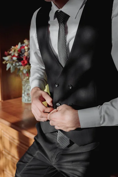 一个穿着白衬衫和灰色背心的男人正站在窗边看着摄像机 手里拿着他的外套 前面的景色一个时髦的手表 男人的风格 — 图库照片