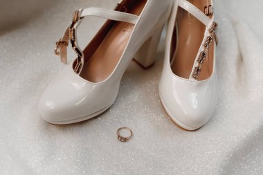 Düğündeki detayların fotoğrafı. Elmas bir nikah yüzüğü zarif kadın ayakkabılarının yanında durur. Dekorlu deri kadın ayakkabıları, yerde.