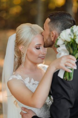 Damat ve gelin ormanda. Ormanda sonbahar düğünü. Mutlu düğün, aşık çift gelini alnından öper. Şık ve güzel. Uzun trenli prenses elbisesi..