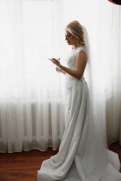 漂亮的金发碧眼的新娘画像 手握鞋带 手握婚礼化妆风格 漂亮的年轻女子穿着白色衣服在家里 — 图库照片