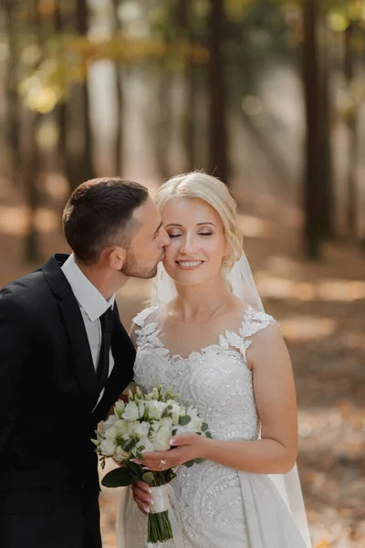 新娘和新郎在森林里的童话般的雾中亲吻着她的脸颊 阳光冲破了浓烟 一个童话般的婚礼 — 图库照片