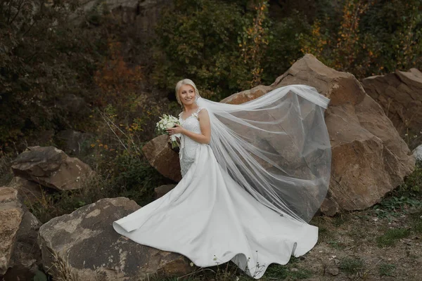 新娘坐在高山上的一块岩石上 旁边是一块大石头 风撕破了面纱 — 图库照片