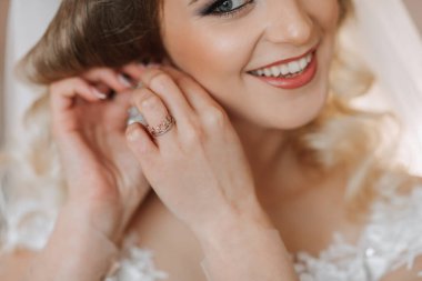 Evdeki düğün töreninden önce küpe takan genç ve güzel bir gelin. Gelinlikli sarışın gelin küpe takıyor.