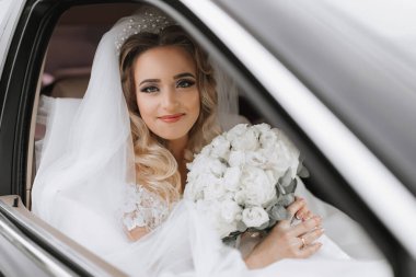 Düğününde siyah bir arabada elinde buketle oturan beyaz saçlı bir gelin. Gelinin portresi. Kalın beyaz dantel elbise.