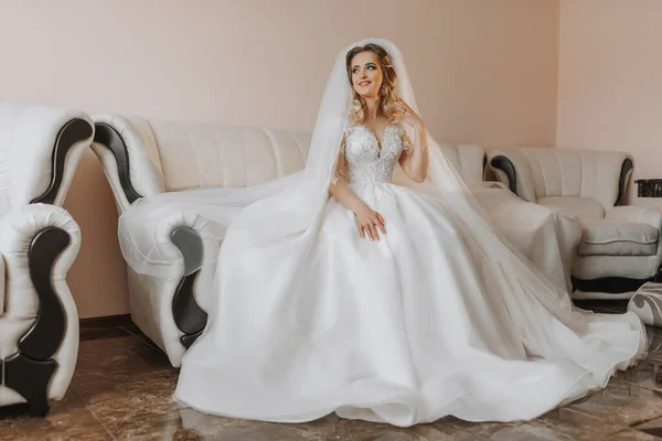 白いウェディングドレスを着た花嫁 幸せな美しいです若いです女性でホワイト伝統的なウェディングドレスで彼女の部屋の革ソファ — ストック写真