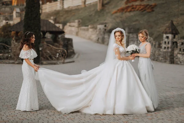 スタイリッシュな新婦付添人は自然に花嫁と楽しみを持っており ドレスの列車で花嫁を助けるためにポーズ — ストック写真