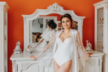 Açık etekli, çıplak bacaklı, açık göğüslü bir gelin Art Nouveau mobilyalarının yanında. Düğün hediyeleri. Saç stilin harika. dantel bornoz,