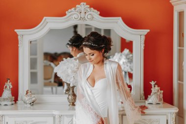 Açık etekli, çıplak bacaklı, açık göğüslü bir gelin Art Nouveau mobilyalarının yanında. Düğün hediyeleri. Saç stilin harika. dantel bornoz,
